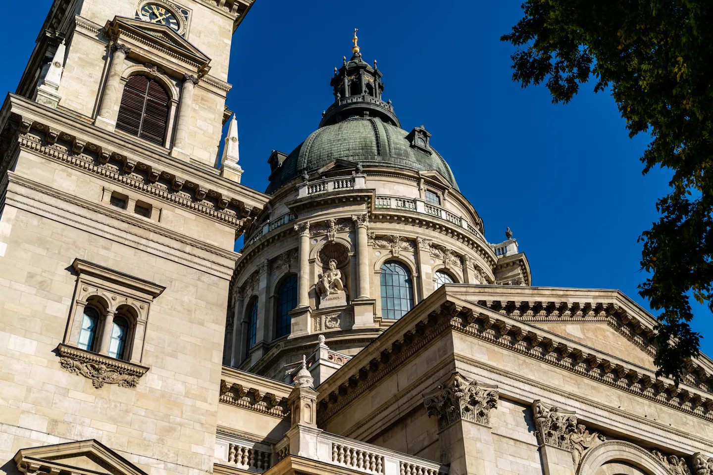 The green dome and bell tower of St Stephen's Basilica in Budapest against a deep blue sky