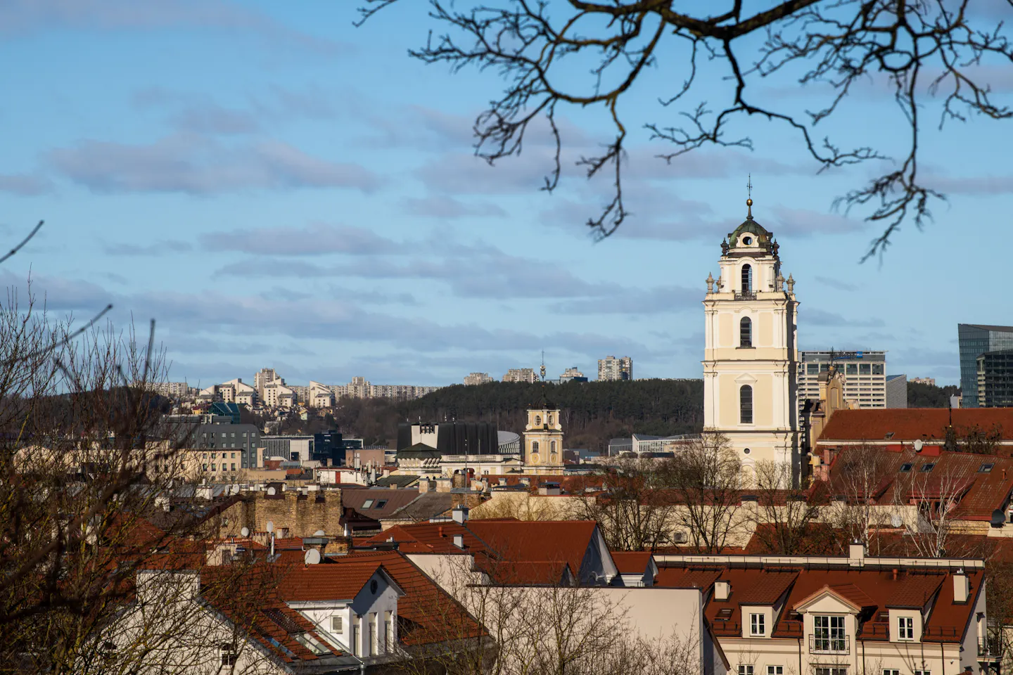 A baroque church bell tower rising above the red-tiled roofs of Vilnius Old Town under a clear blue sky