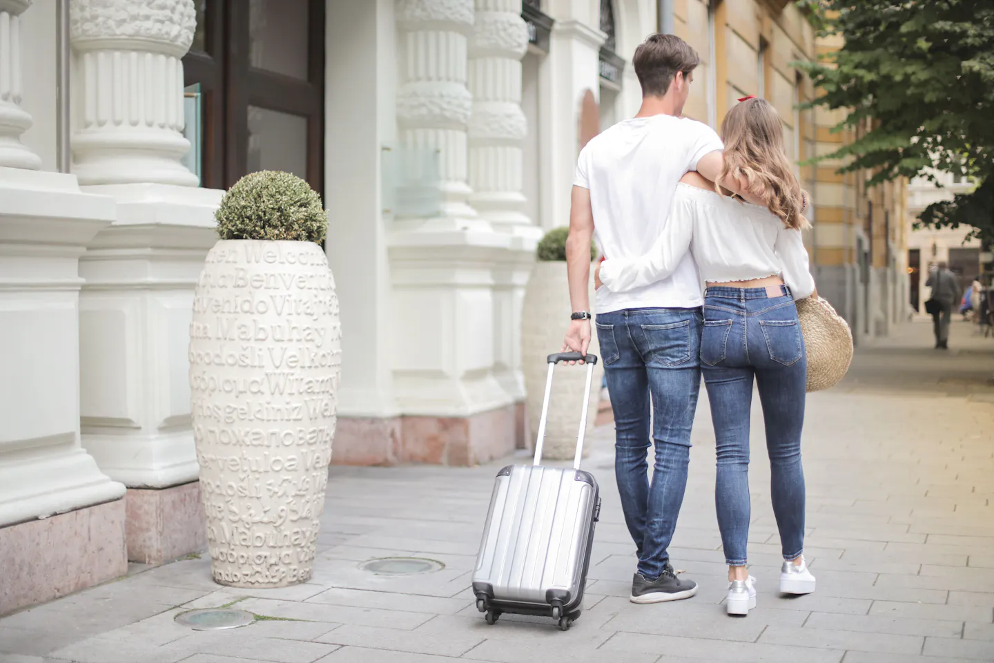 Couple walking along a city sidewalk with a rolling suitcase