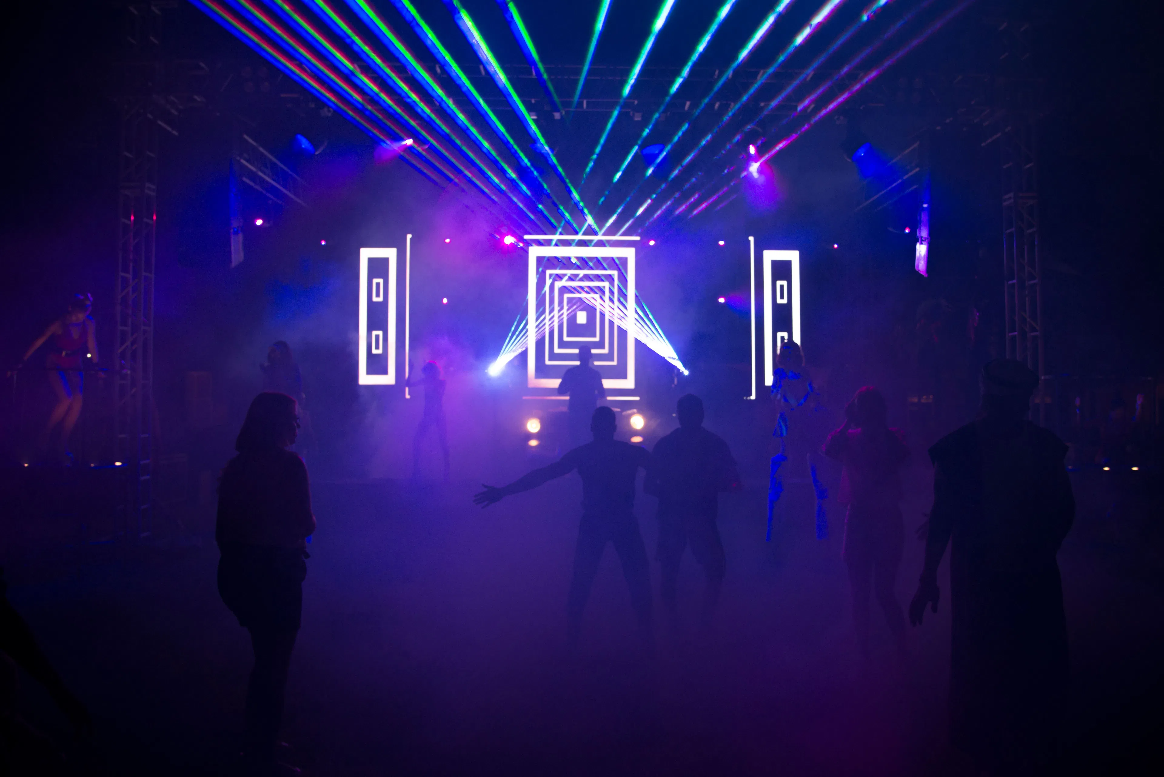 Silhouetted crowd dancing under blue and green laser beams and smoke in a dark nightclub