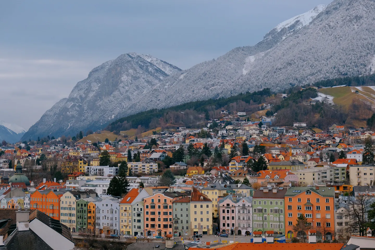 Brightly coloured rooftops of Innsbruck packed below a vast snow-streaked mountain wall
