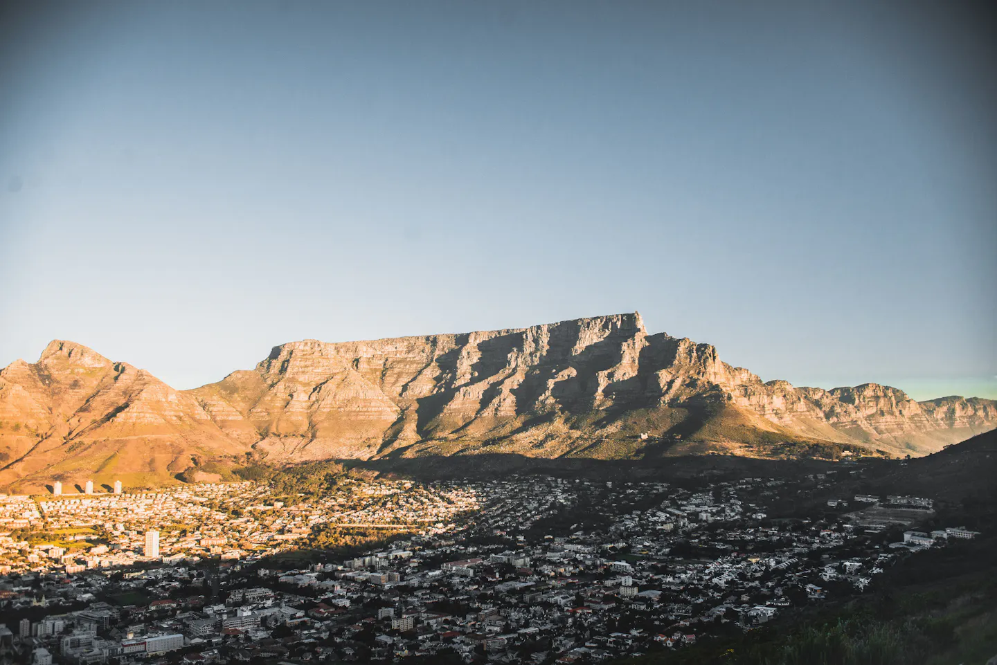 The flat summit and buttressed cliffs of Table Mountain catching late sun above the rooftops of Cape Town