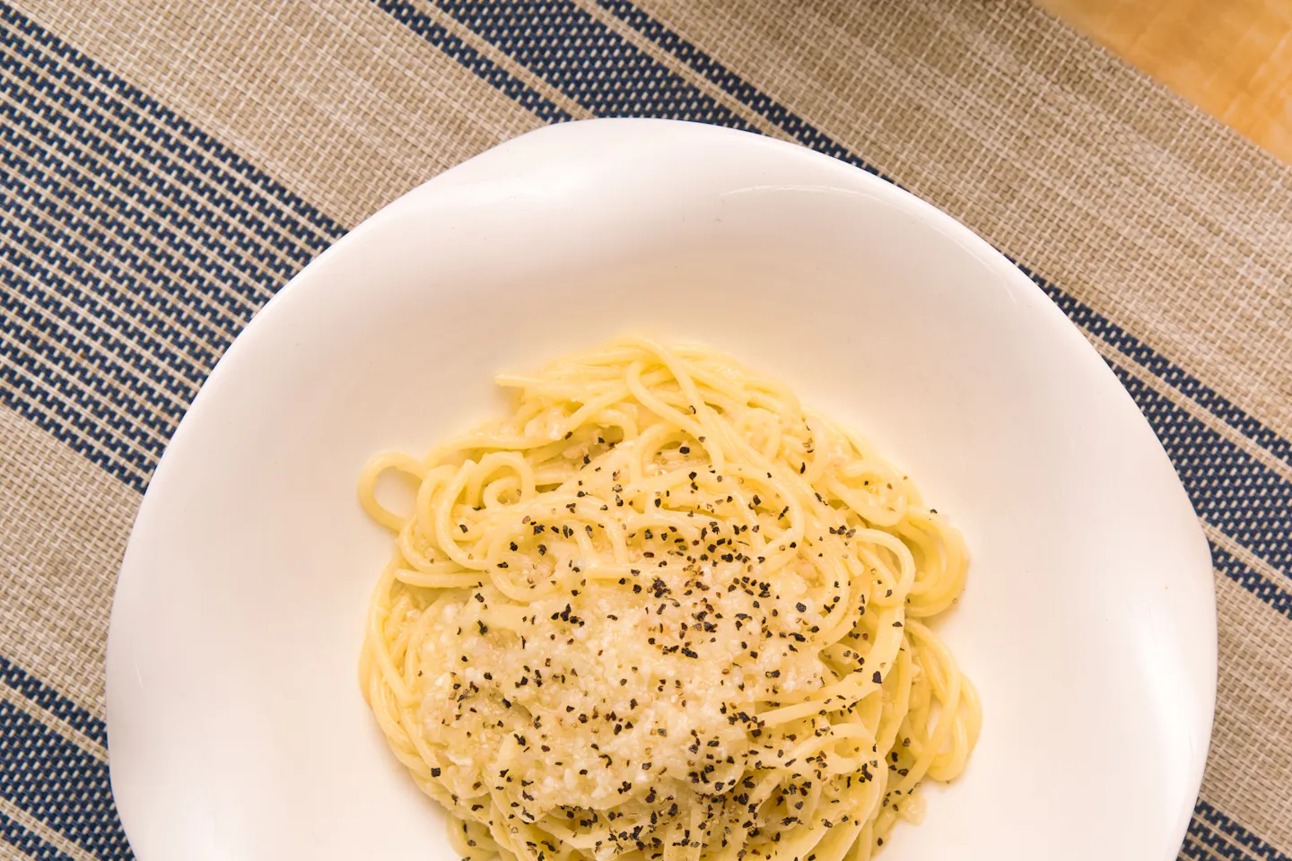 A white bowl of cacio e pepe, spaghetti coated in melted pecorino and coarsely ground black pepper