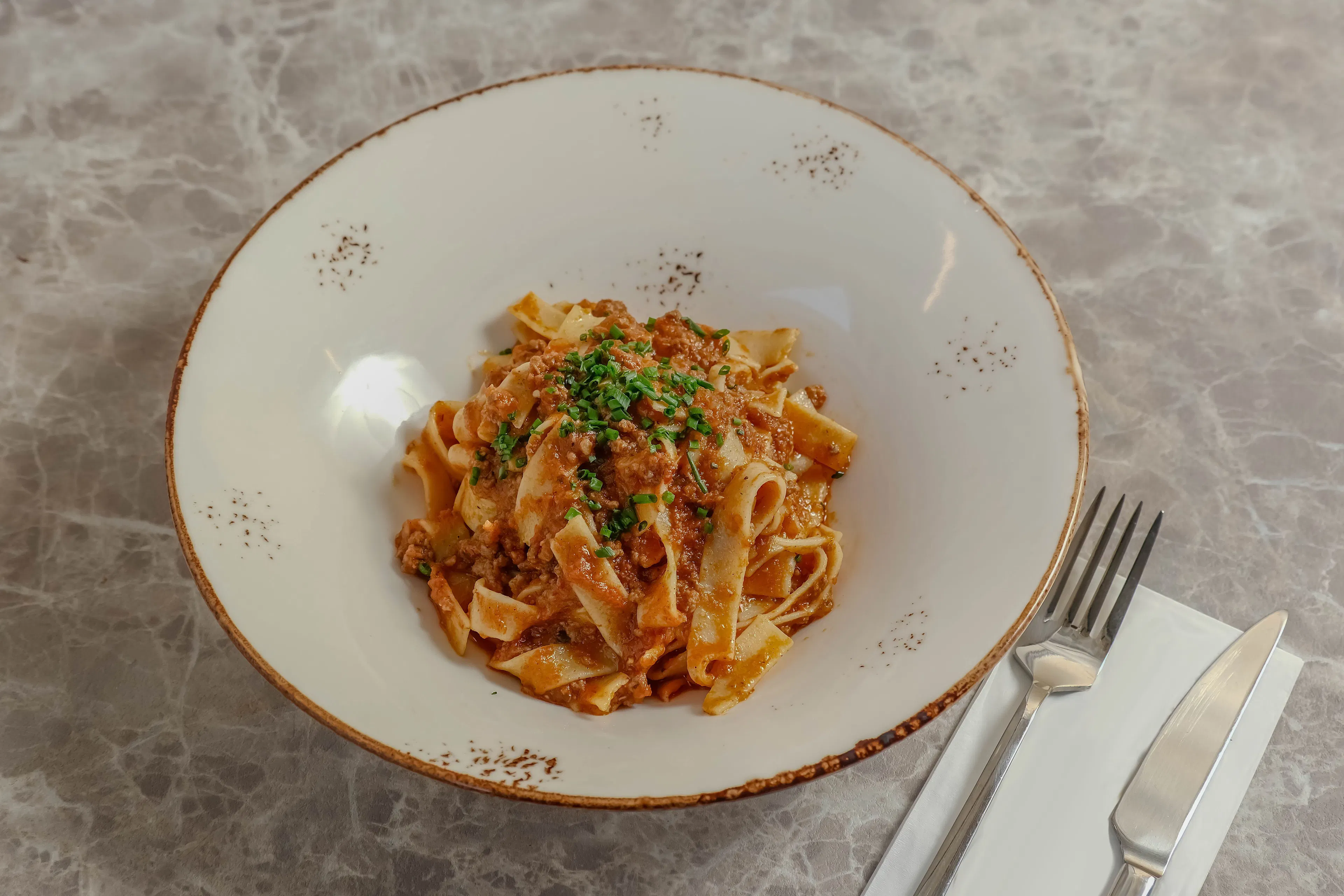 A bowl of fresh tagliatelle in a rich meat ragu on a marble table