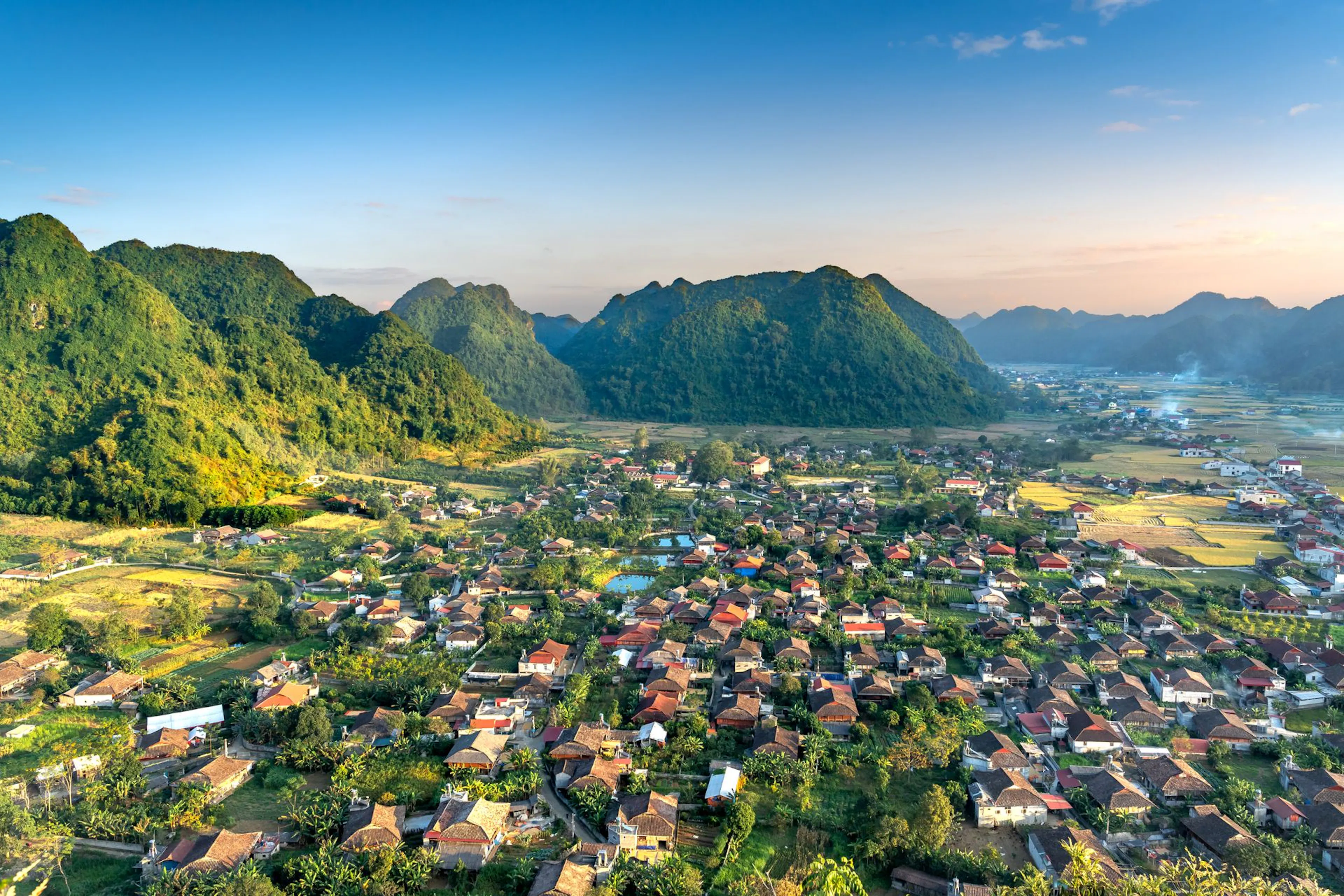 Aerial view of a valley town and rice fields framed by forested mountains in Vietnam at golden hour