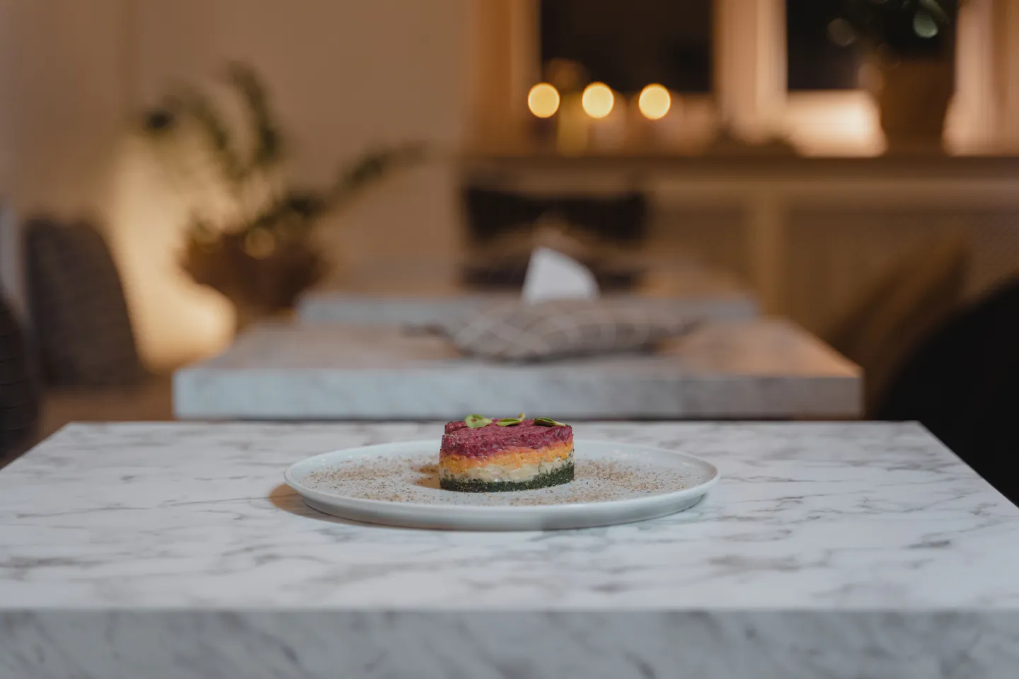 A small carefully plated dish alone on a marble table in a warm candlelit dining room