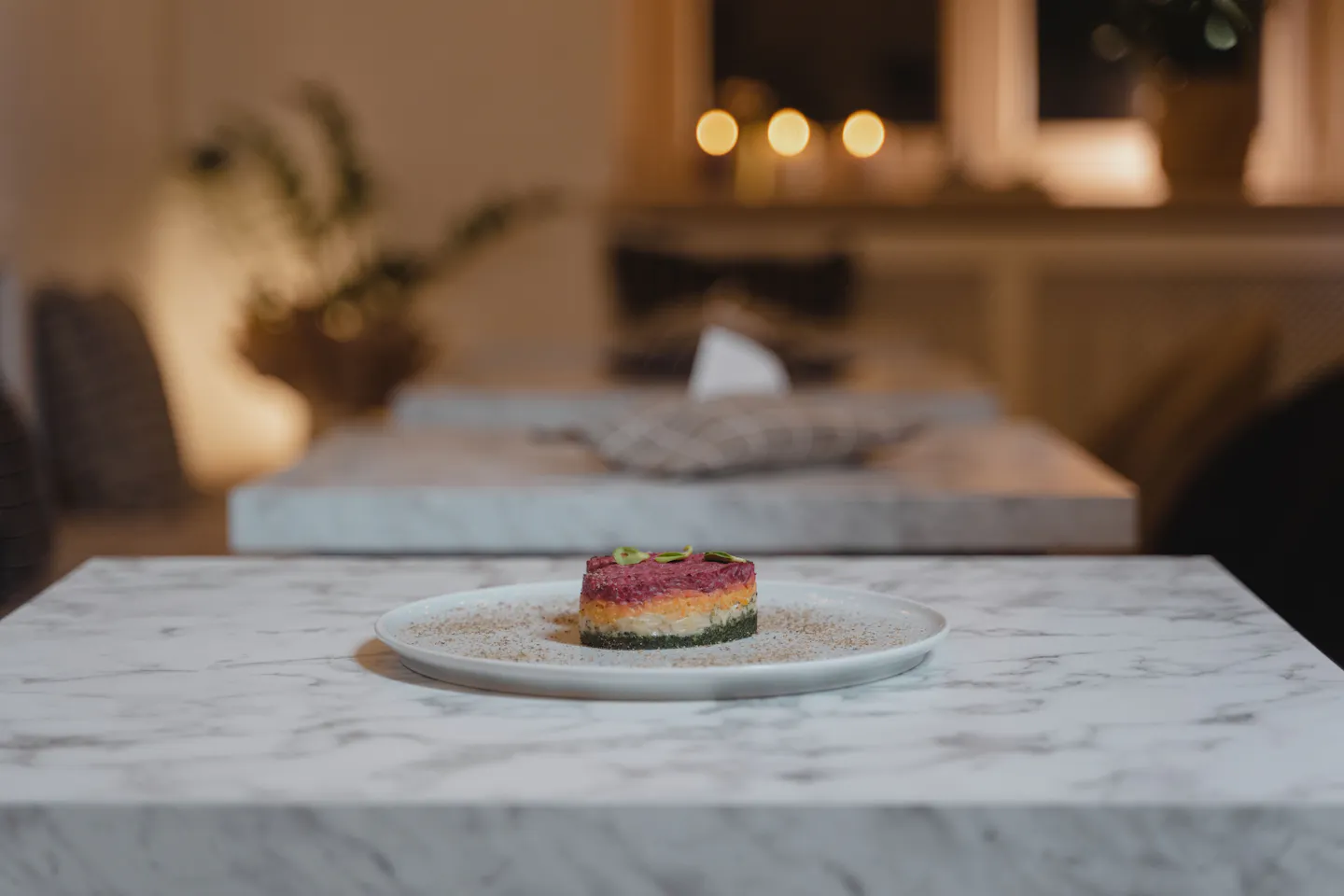 A small carefully plated dish alone on a marble table in a warm candlelit dining room