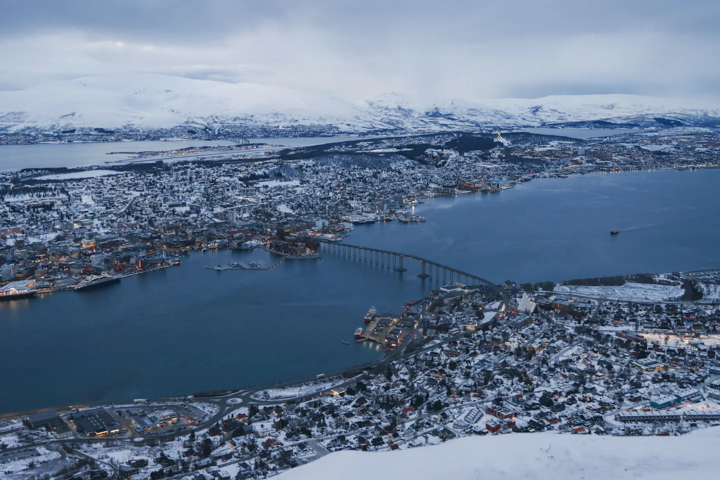 Tromso lit up under deep blue polar twilight with snow on the surrounding mountains