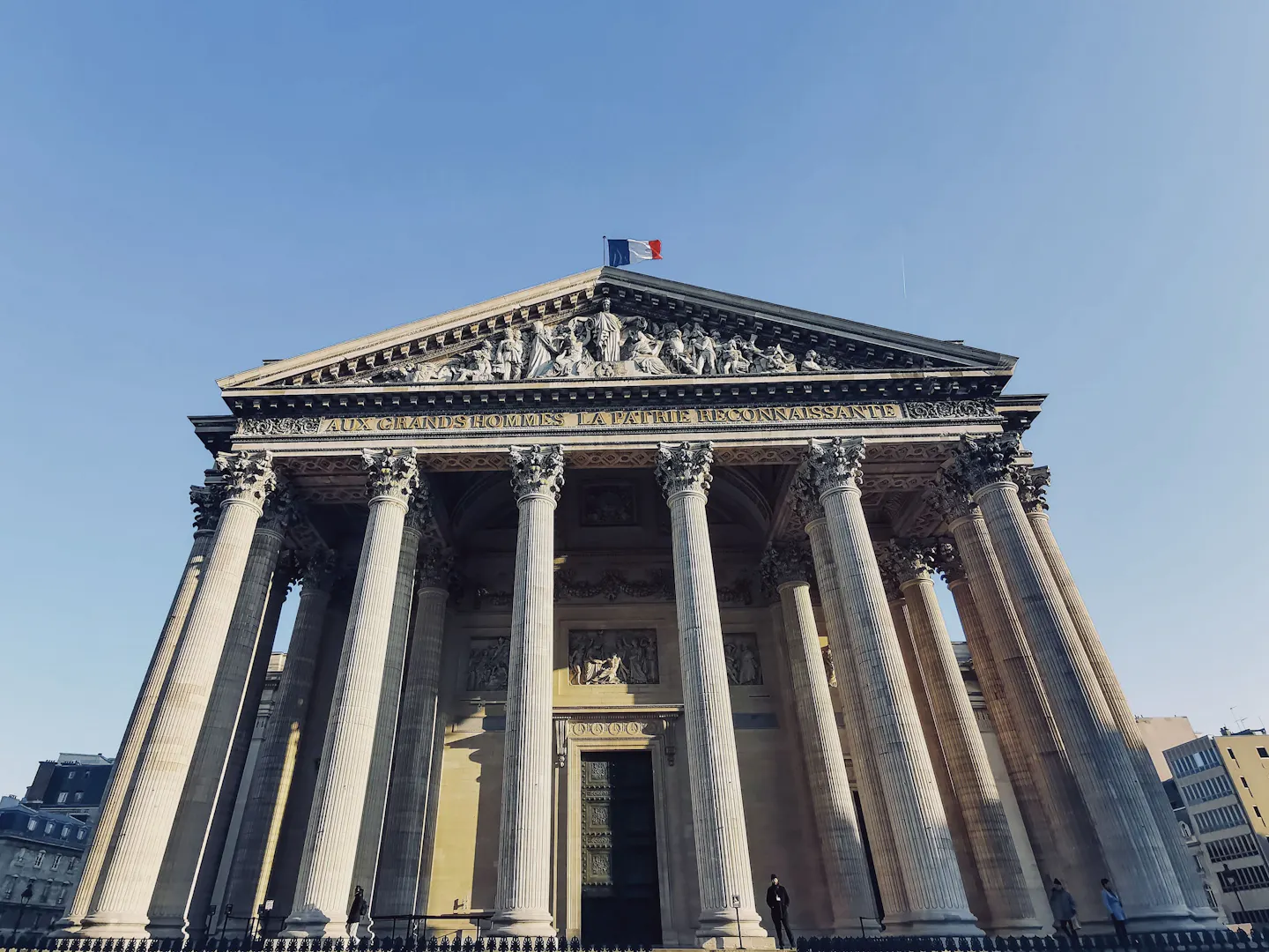 The columned portico and dome of the Pantheon in Paris seen from below against a clear blue sky