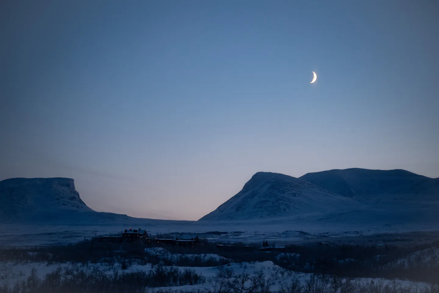 The U-shaped Lapporten valley and snow-covered peaks above Abisko under a clear twilight sky with a crescent moon