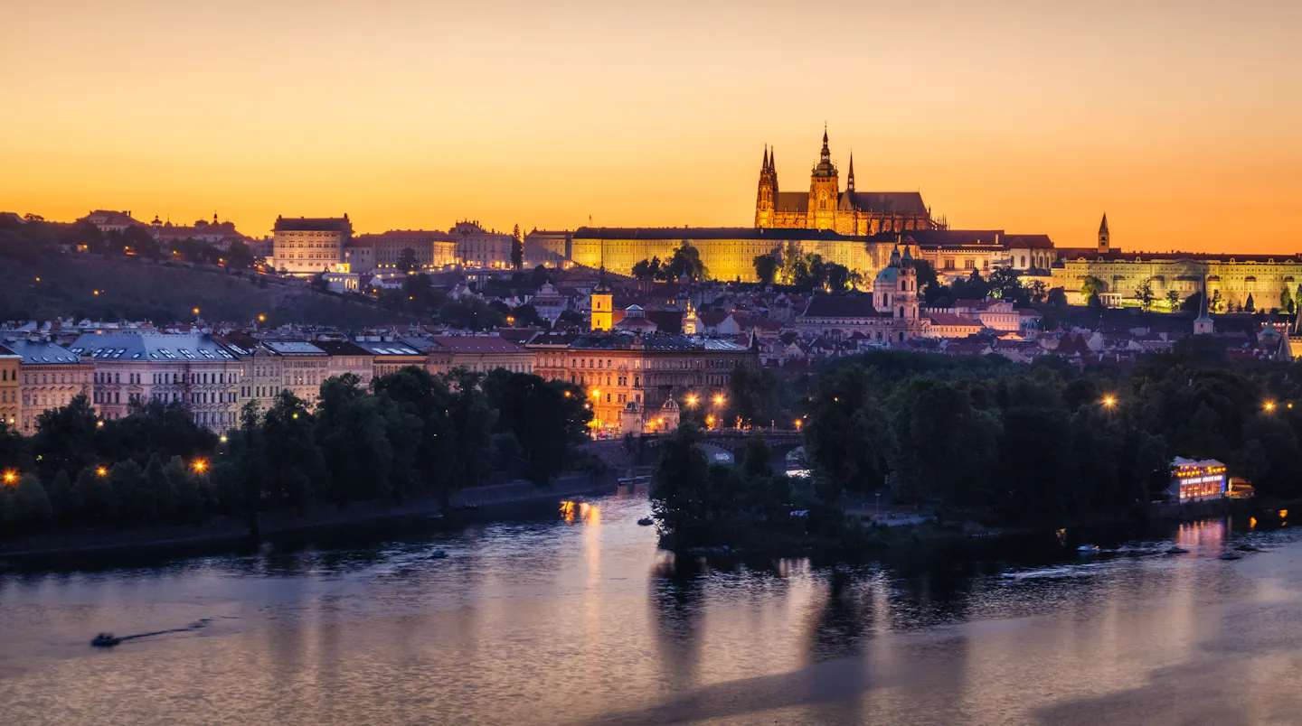 Prague Castle and St Vitus Cathedral lit above the Vltava under a deep orange evening sky