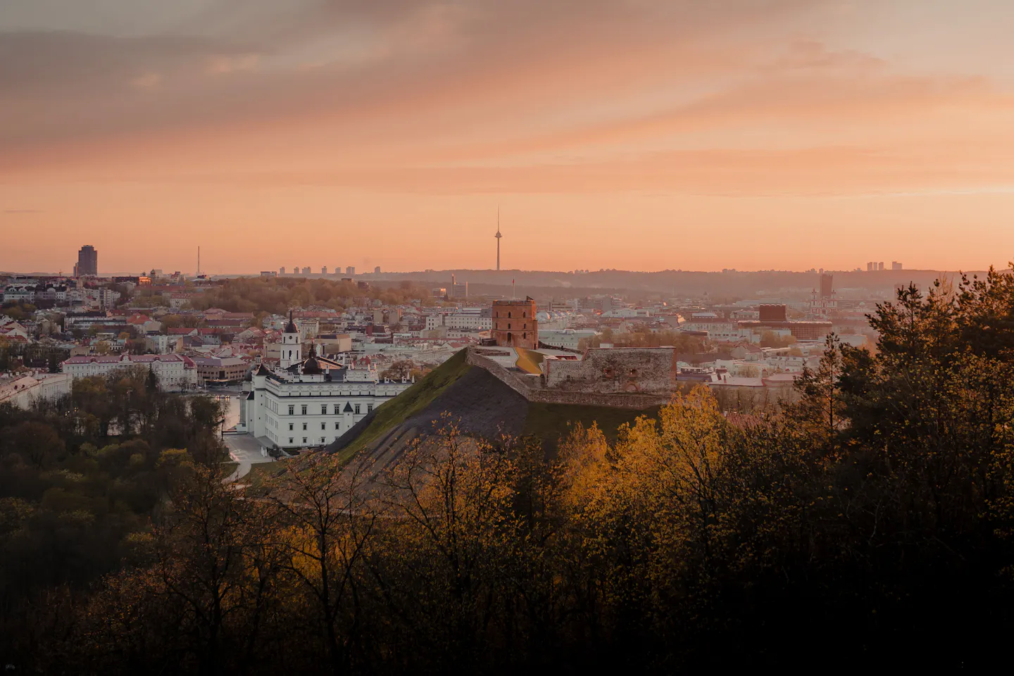 Gediminas Tower on its green hill above the Old Town of Vilnius under a pink sunset sky