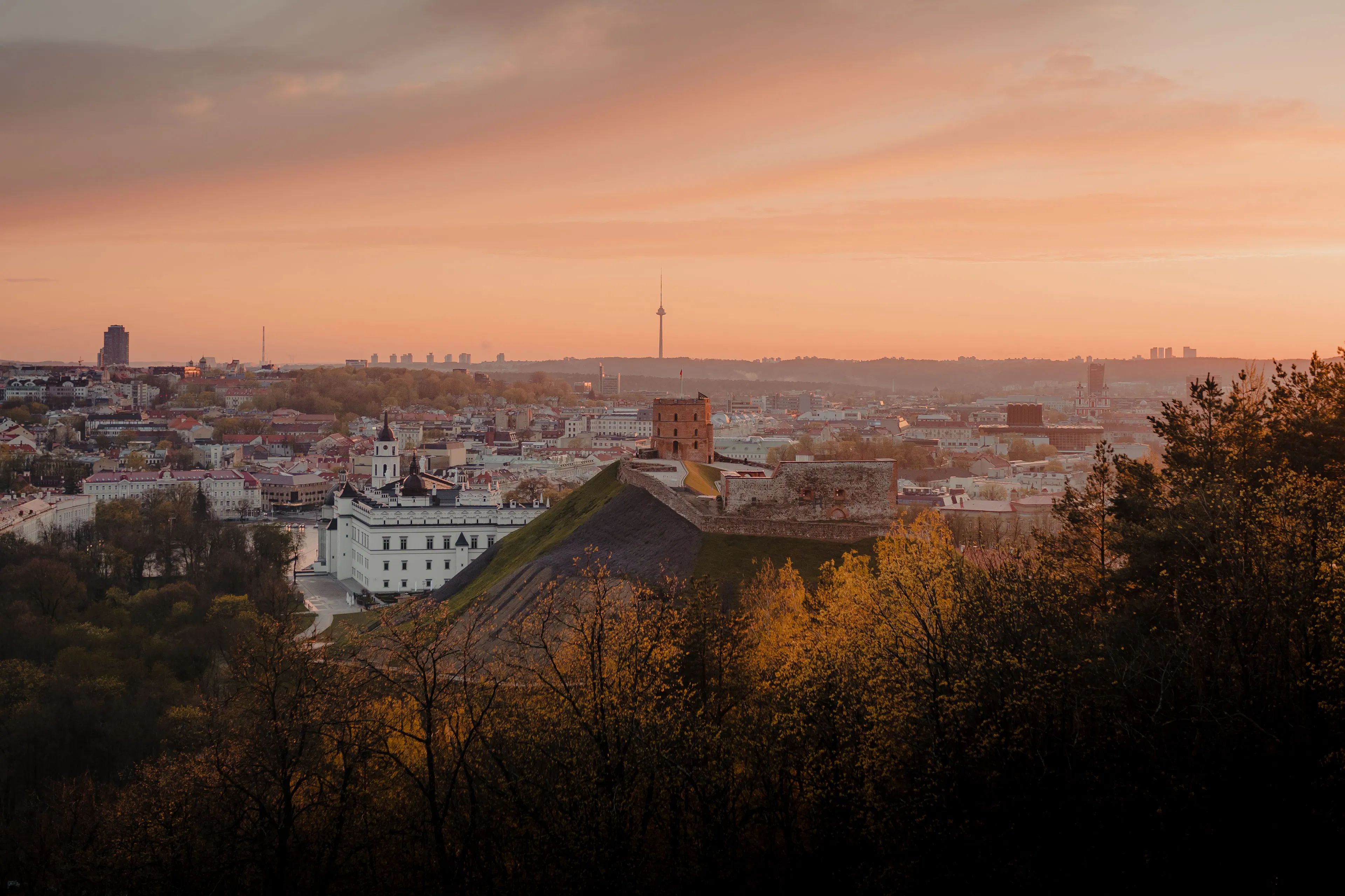 Gediminas Tower on its green hill above the Old Town of Vilnius under a pink sunset sky
