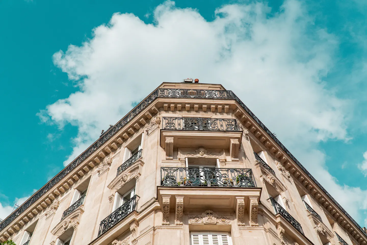 The corner of a Haussmann apartment building with wrought-iron balconies, seen from below against a deep blue sky