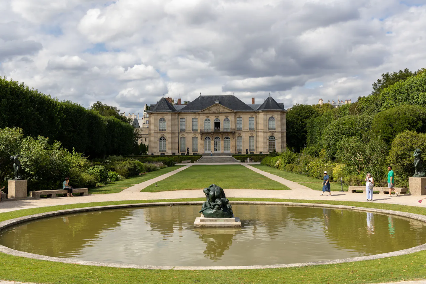 The Hotel Biron mansion and the circular pond of the Musee Rodin garden under a cloudy summer sky