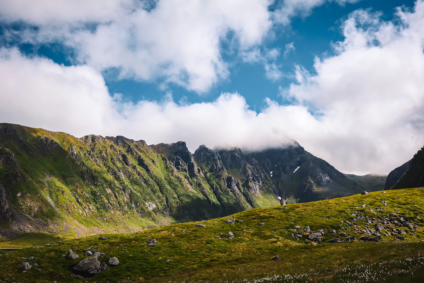 Green mountain ridges half-wrapped in tall white summer clouds above open grassland on the northern Norwegian coast