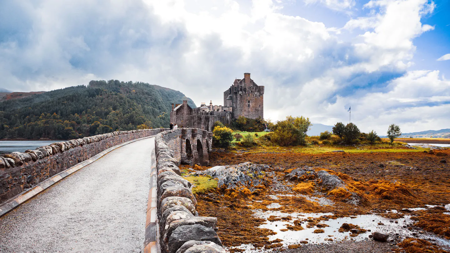 Eilean Donan Castle at the end of its stone bridge, with autumn seaweed and wooded hills