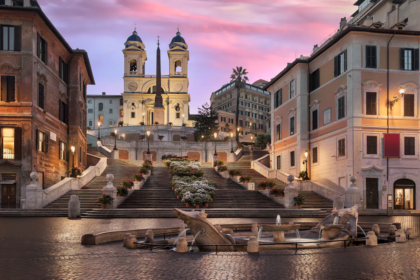 The Spanish Steps and the twin towers of Trinita dei Monti under a pink dawn sky, with the Barcaccia fountain in the empty square below