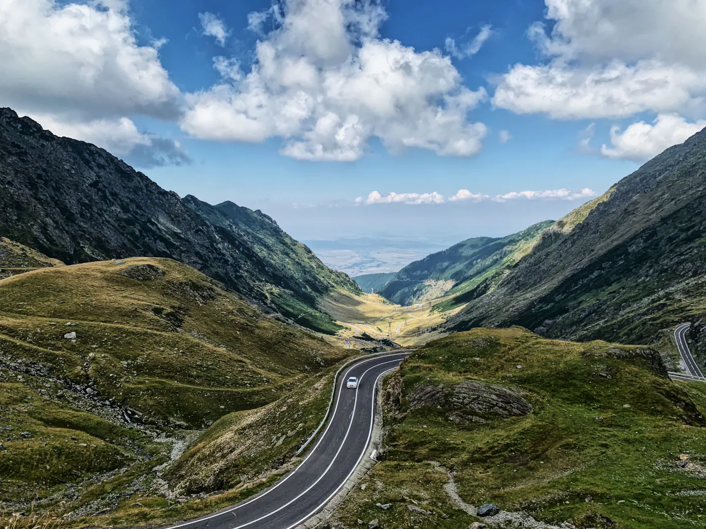 A winding mountain road descending through a green alpine valley under a bright blue sky
