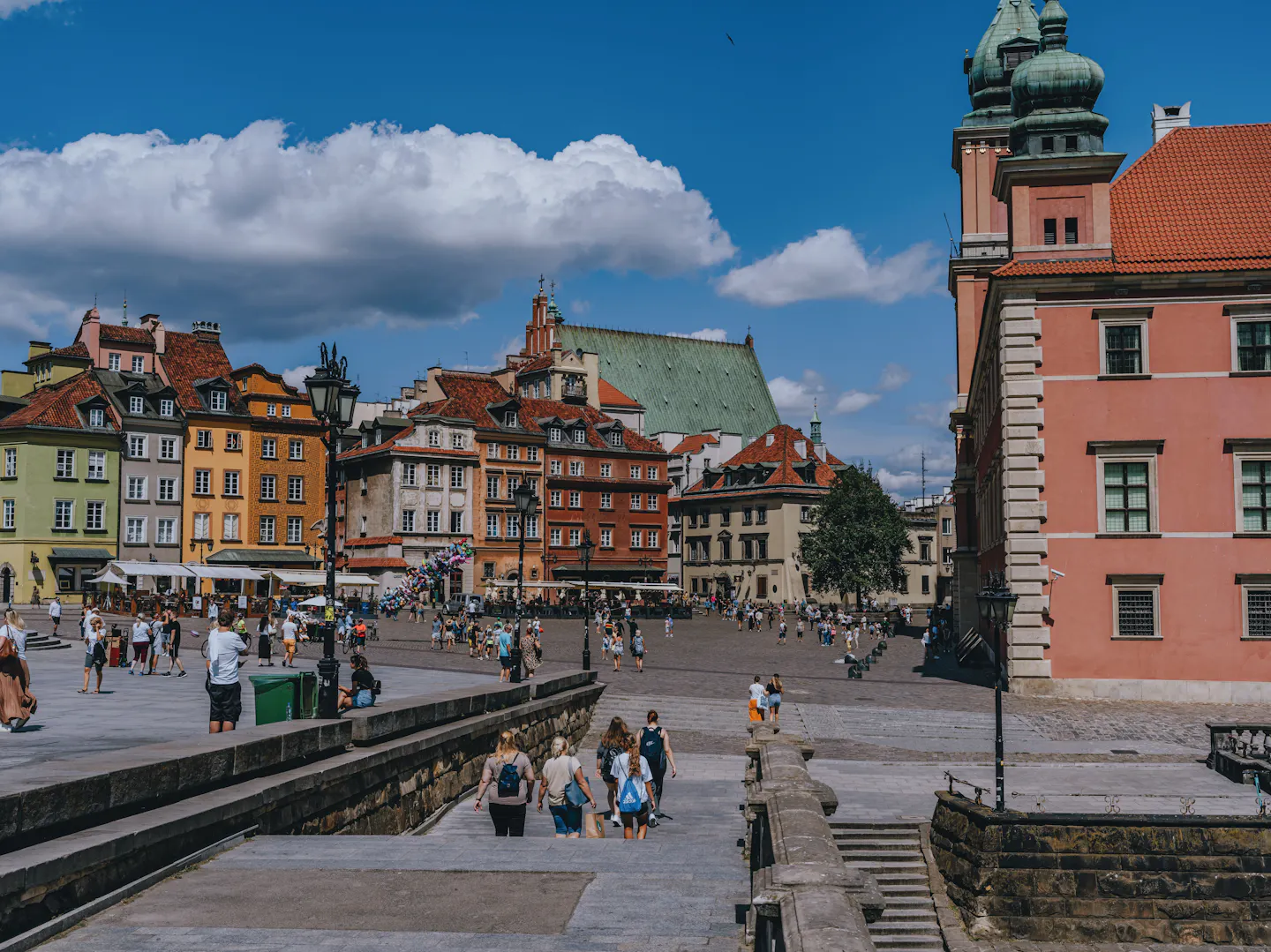 Sunny Castle Square in Warsaw's Old Town, with colourful townhouses, the Royal Castle and people strolling