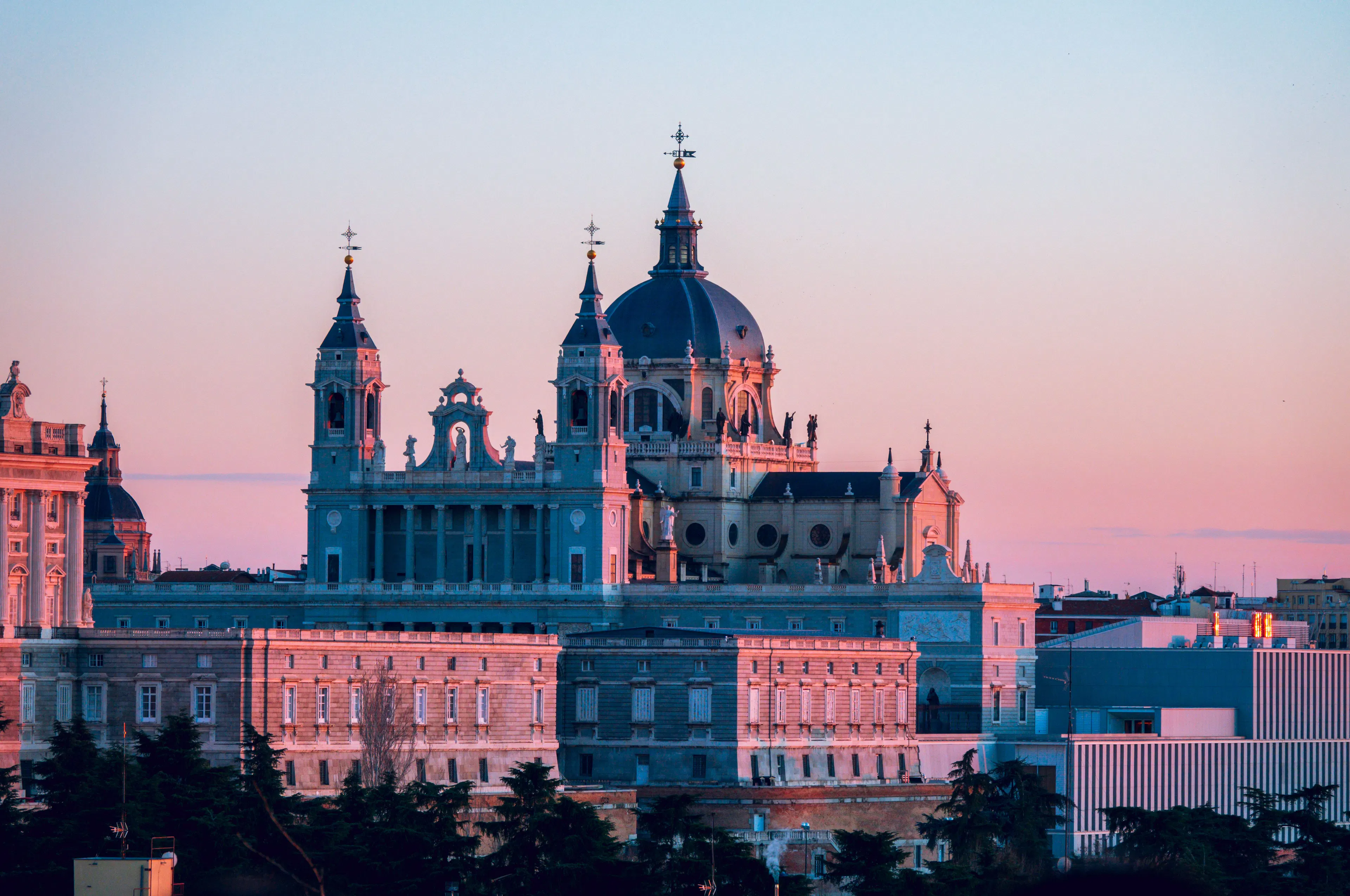 The domes and spires of Almudena Cathedral and the Royal Palace of Madrid catching pink light at sunset