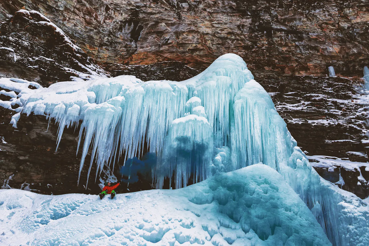 A climber beneath towering frozen waterfalls in a snowy canyon in Banff National Park, Canada.