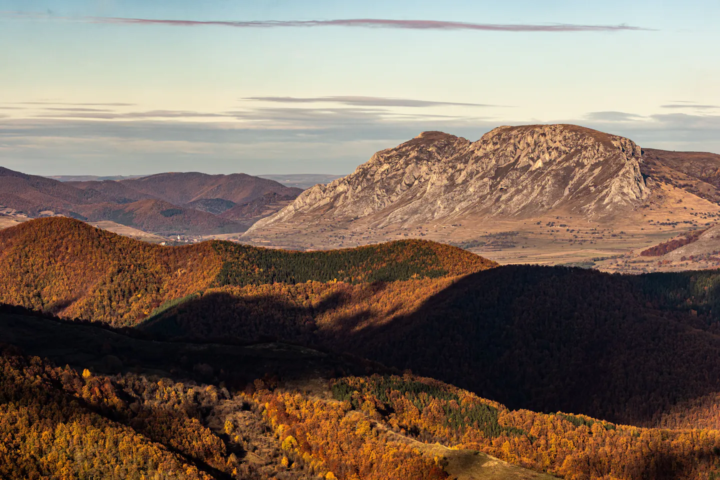 Golden autumn forests rolling below a pale limestone ridge in the Carpathian hills of Transylvania at sunset