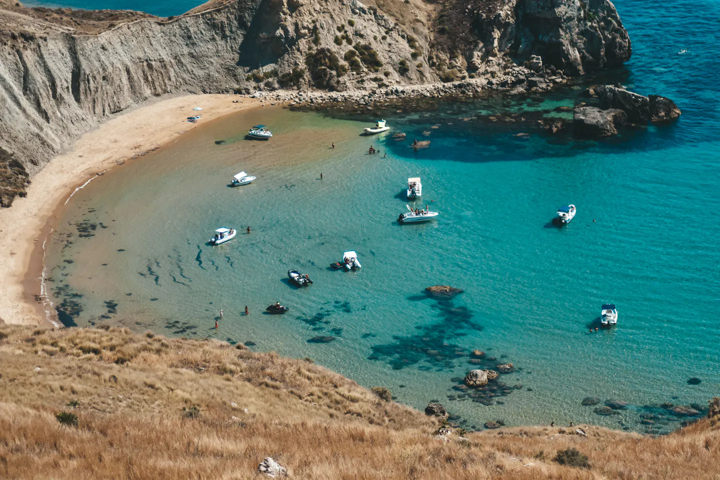 Boats anchored in a sheltered turquoise cove with a sandy crescent on the southern Italian coast