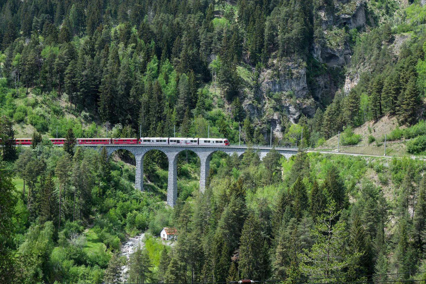 A red train crossing the curved stone arches of the Landwasser Viaduct above a forested Swiss gorge