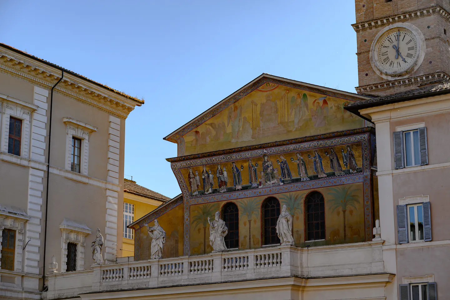 The gold mosaic frieze and brick bell tower of the basilica of Santa Maria in Trastevere against a clear blue sky