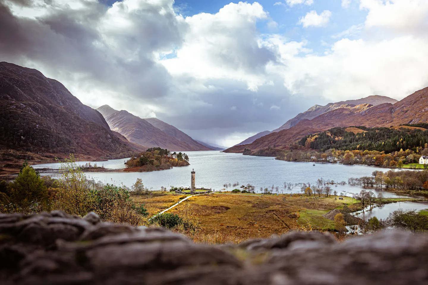 Loch Shiel and the Glenfinnan Monument beneath rust-coloured Highland mountains and dramatic autumn clouds