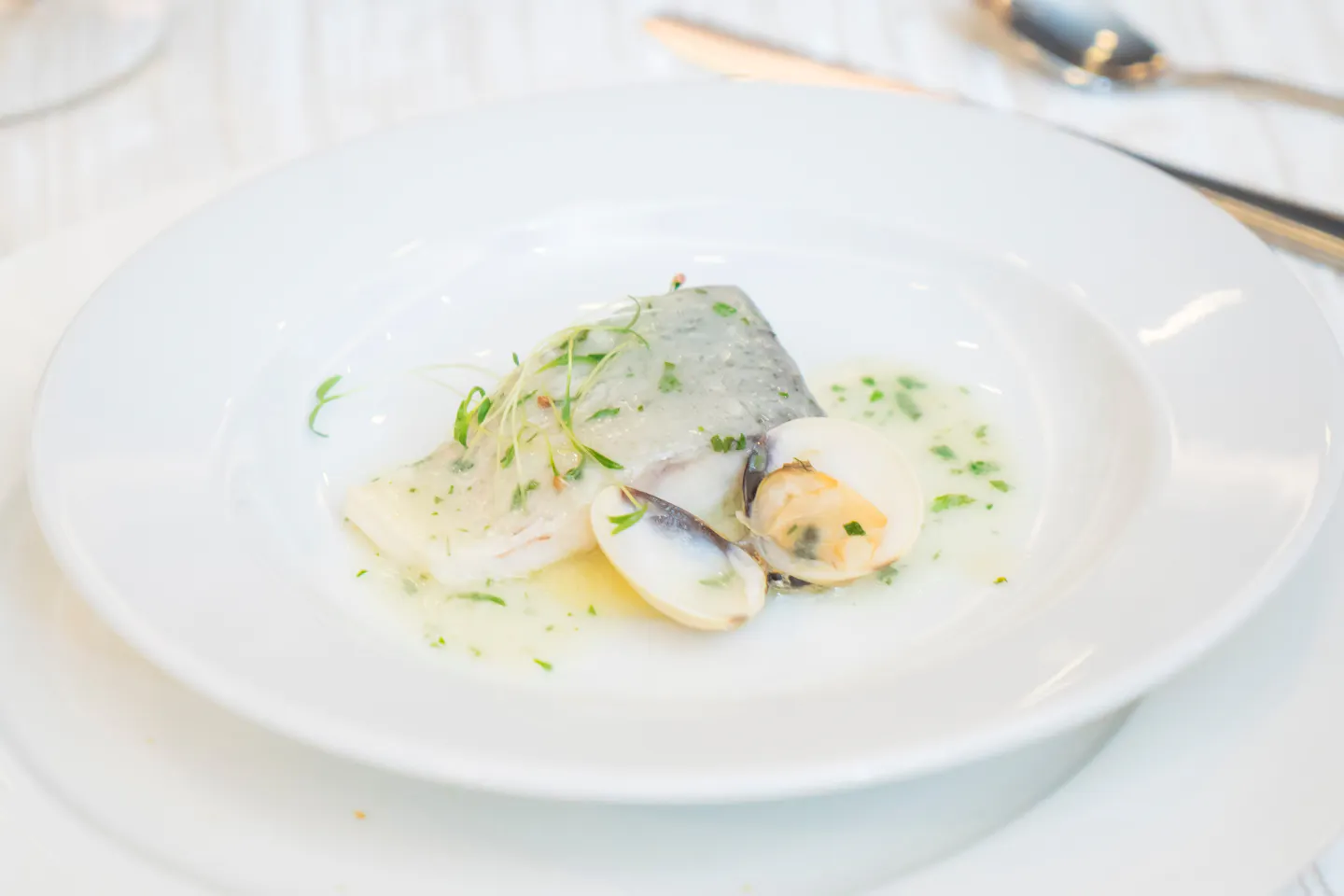 A fillet of white fish with clams in a herb and olive-oil broth on a white plate