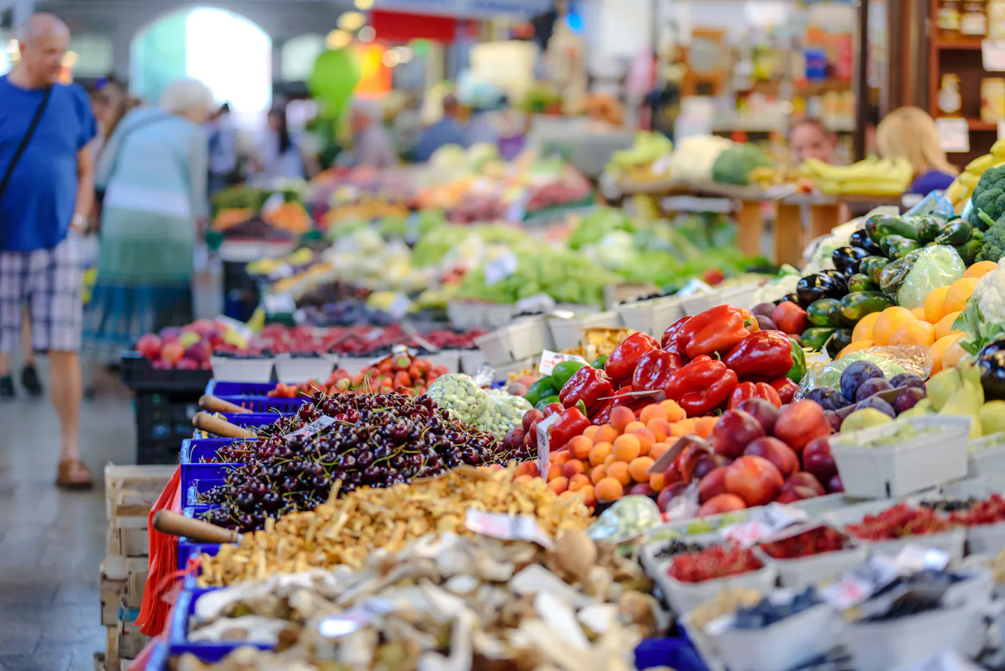Market stalls piled with peppers, cherries, apricots, mushrooms and vegetables in a covered food hall