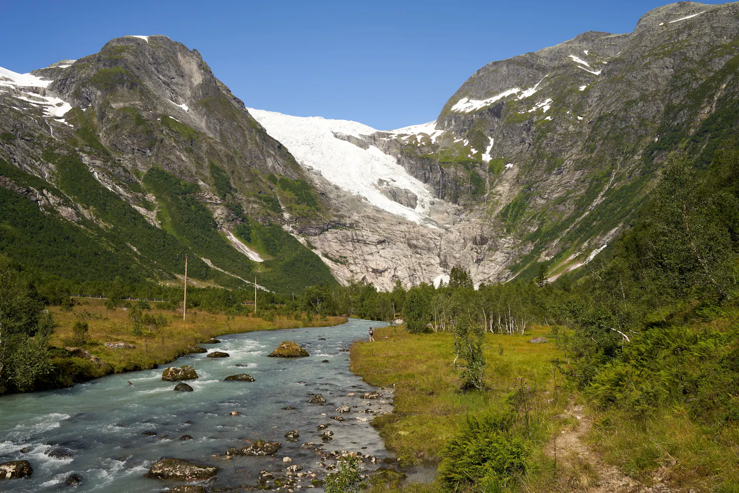 A pale glacier hanging above a steep Norwegian valley with a fast rocky river running through it