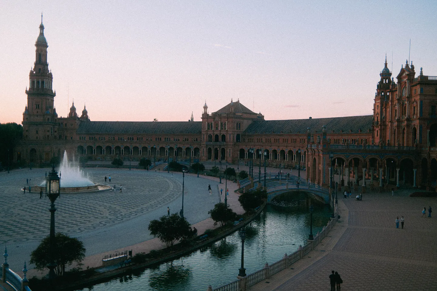 The curved arcade, canal and fountain of the Plaza de Espana in Seville under a pink dusk sky