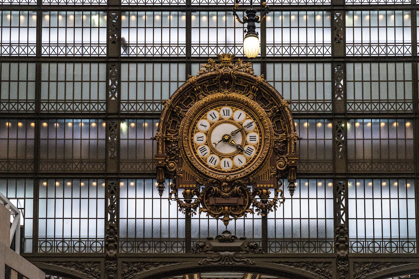 The gilded station clock of the Musee d'Orsay set against the museum's glazed wall