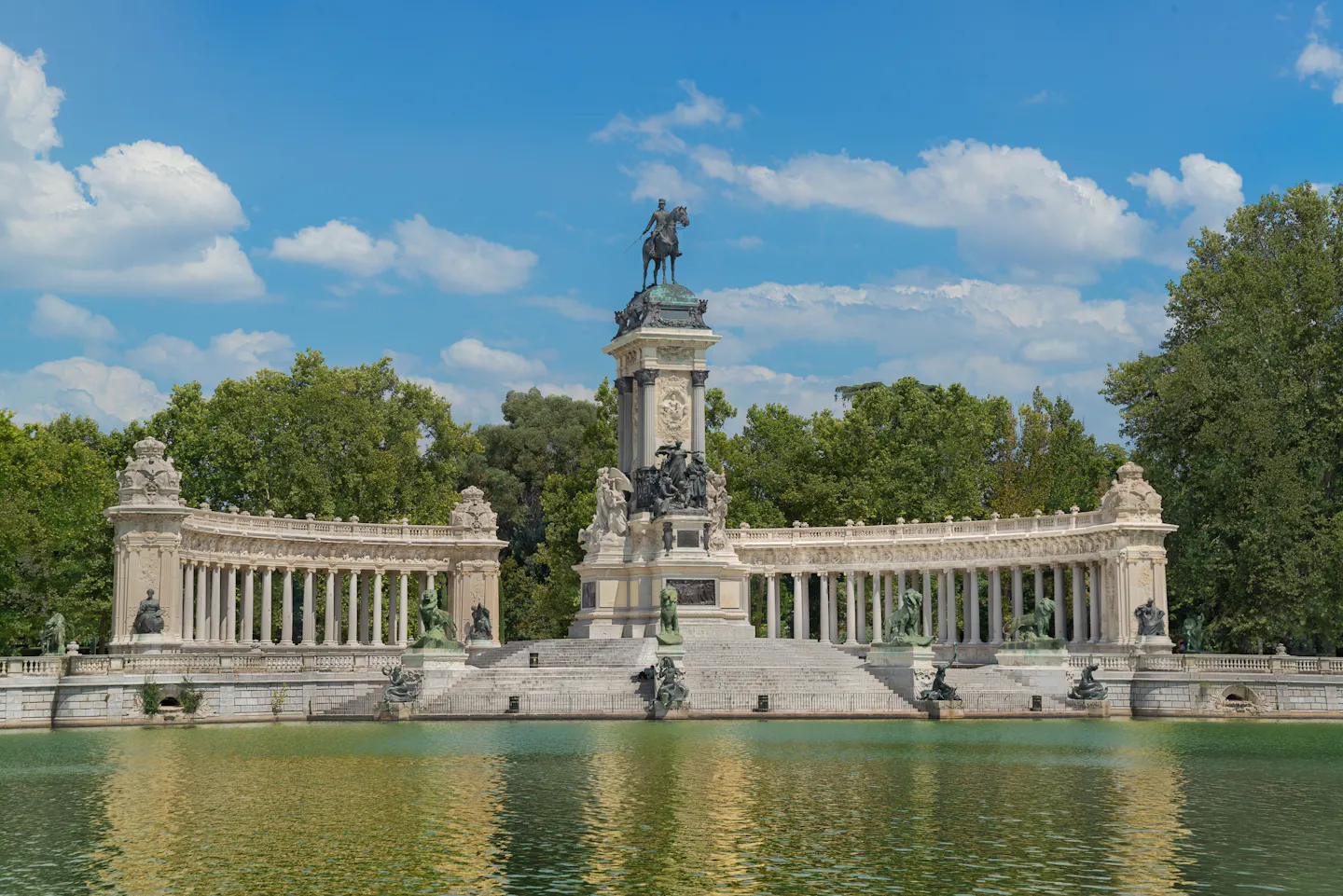 The colonnaded Monument to Alfonso XII reflected in the boating lake at Retiro Park under a blue sky