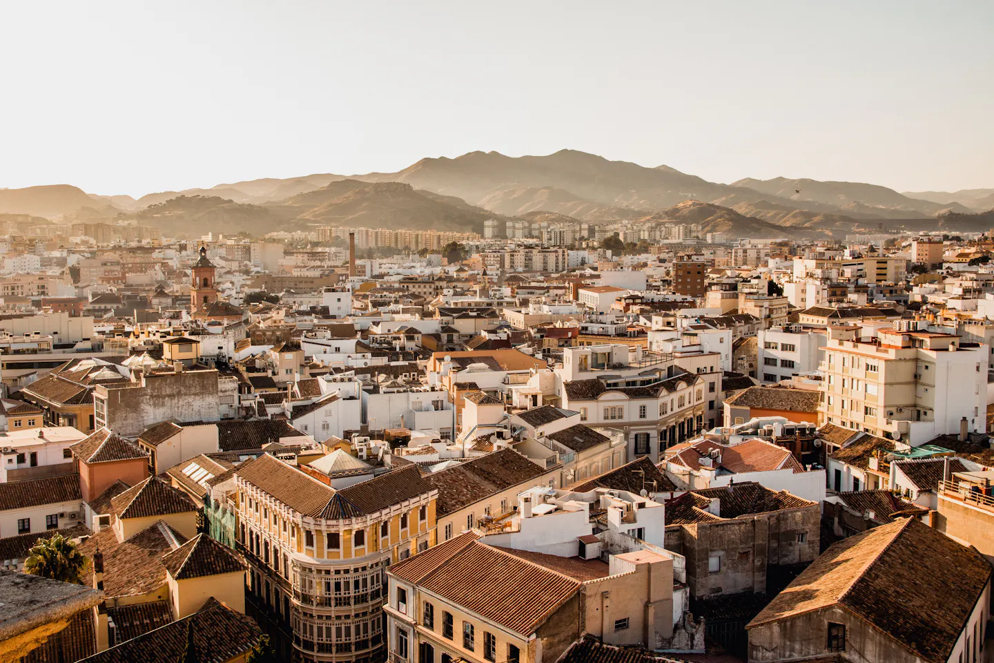 Warm evening light over the tiled rooftops of Malaga with hills rising behind the city
