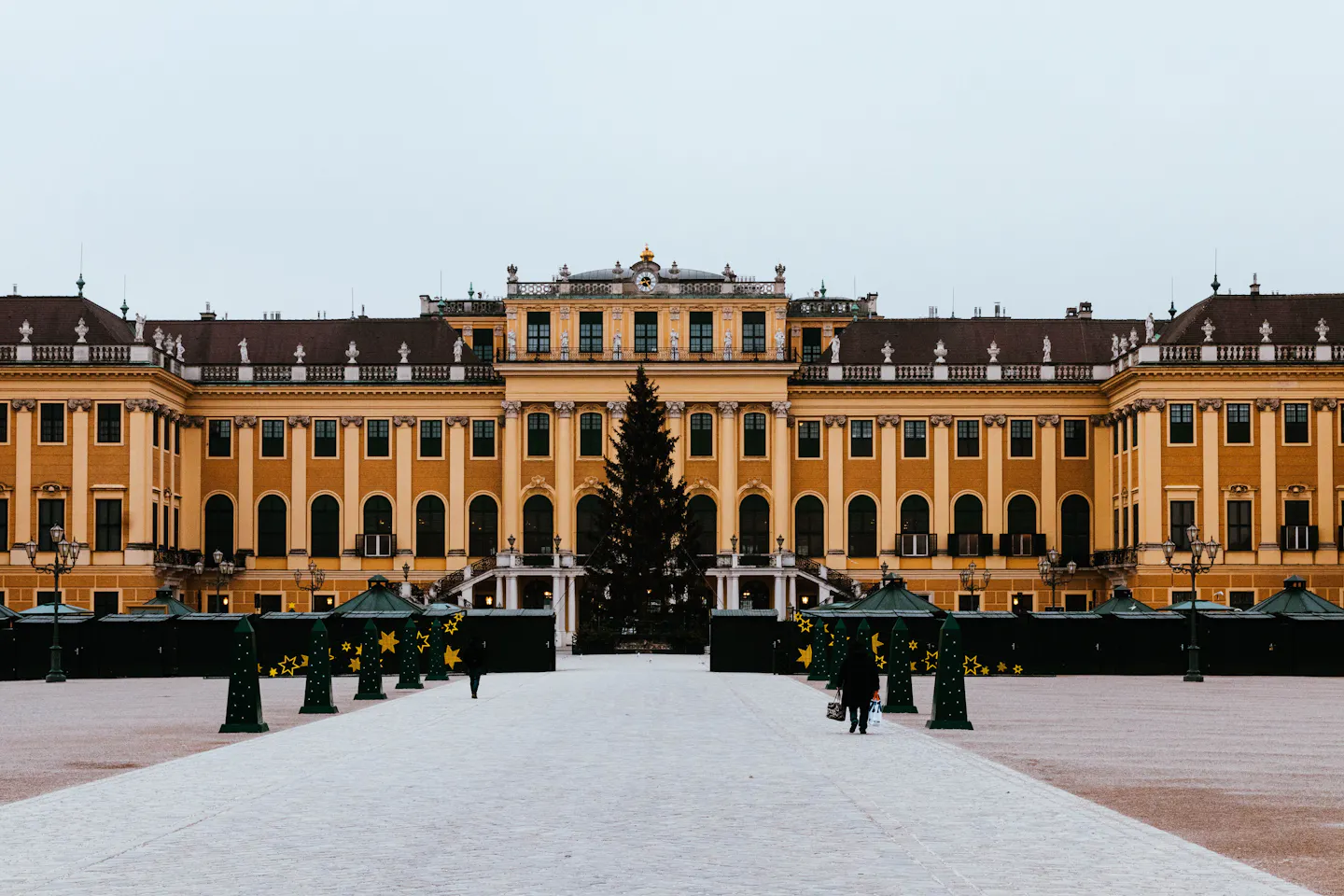 Schonbrunn Palace in Vienna behind a Christmas tree and market huts on a winter day