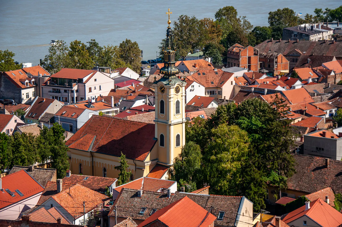 Sunlit terracotta rooftops of Belgrade's old riverside quarter, with a pale yellow baroque bell tower rising among the houses and the Danube behind
