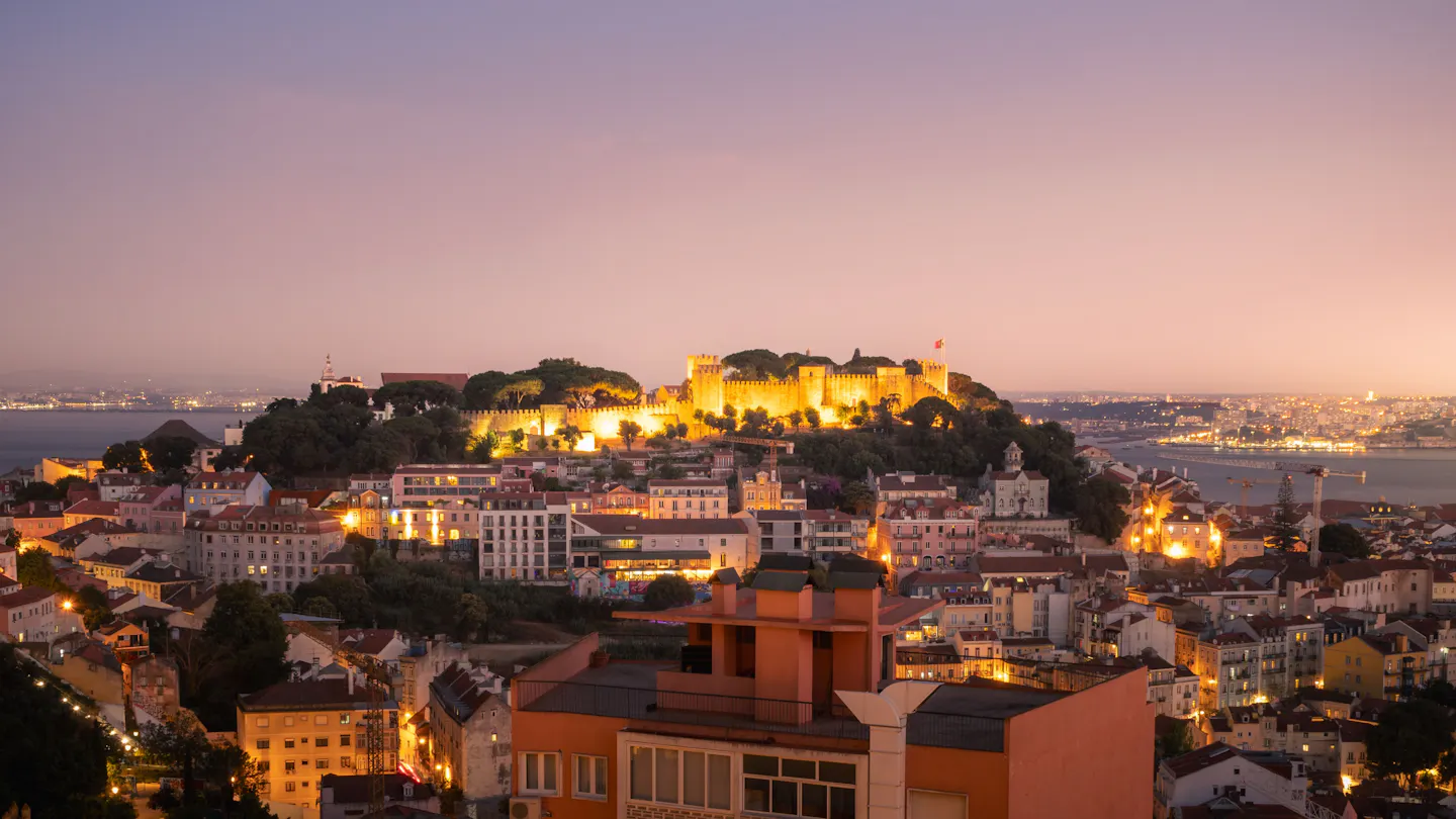 Sao Jorge Castle lit on its hill above Lisbon's rooftops under a pink twilight sky