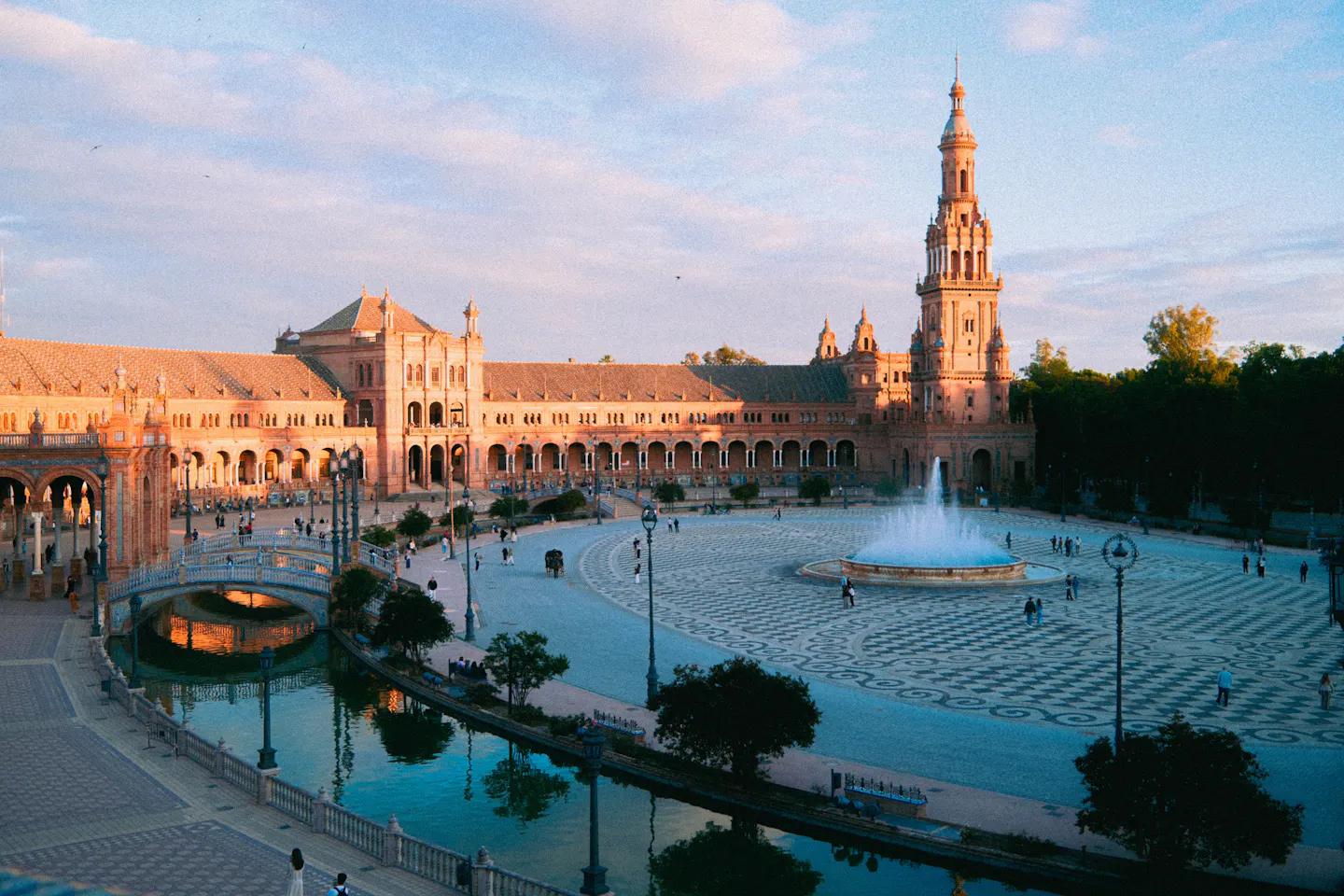 Seville's Plaza de España at golden hour, with its tower, fountain, canal and tiled bridge in warm light
