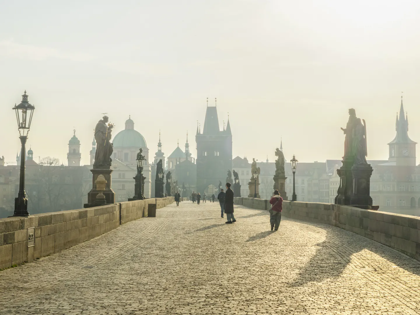 Statues along Charles Bridge in Prague in golden morning mist with the Old Town bridge tower ahead