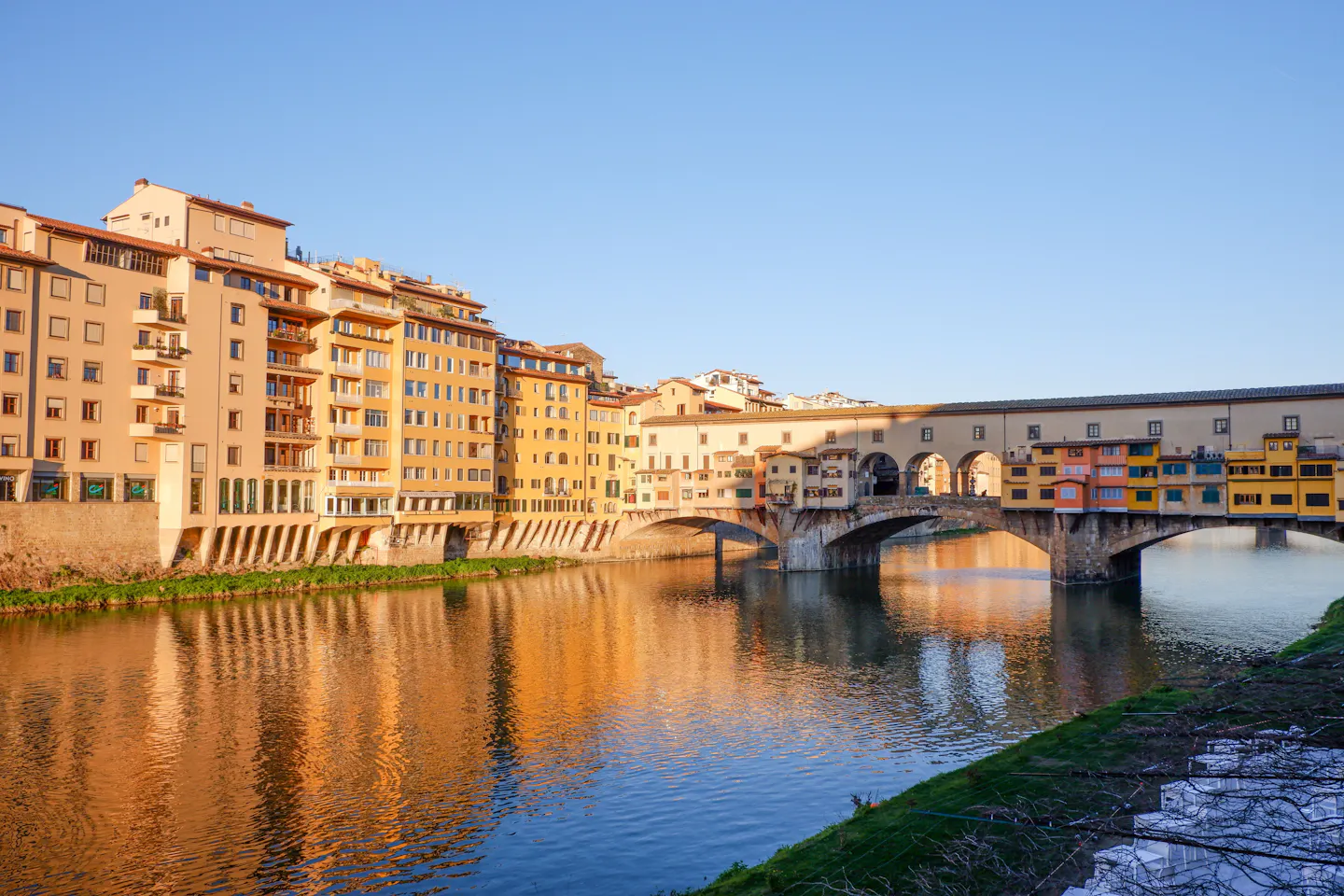 The Ponte Vecchio and its shops reflected in the Arno in Florence in warm evening light