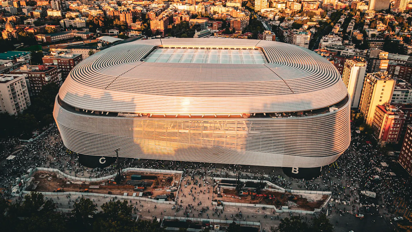 Aerial view of the Santiago Bernabeu stadium glowing in golden evening light with the streets of Madrid around it