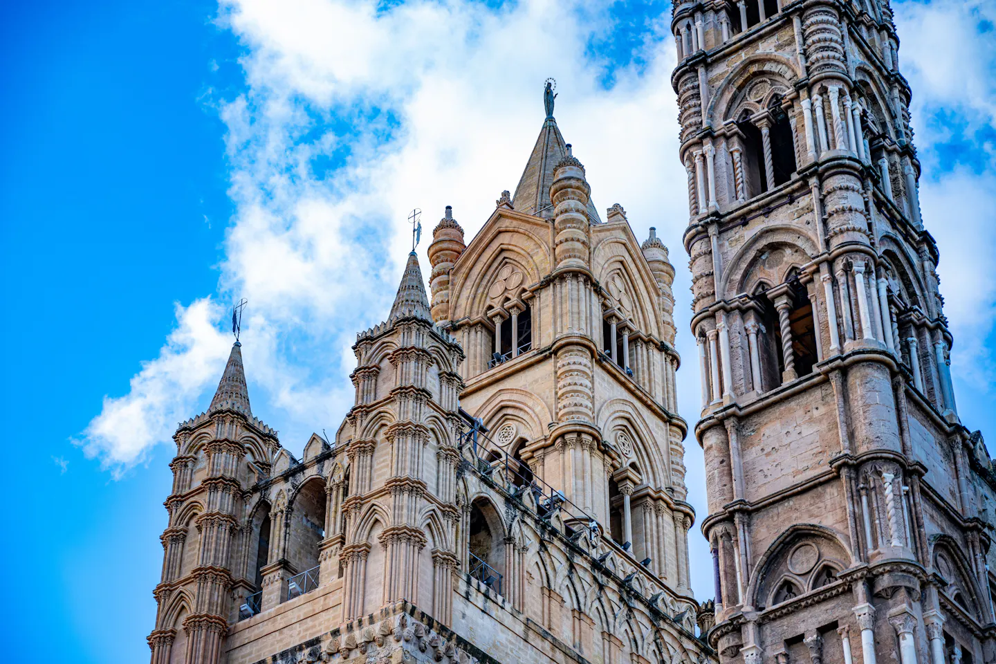The carved stone towers and spires of Palermo Cathedral against a vivid blue sky