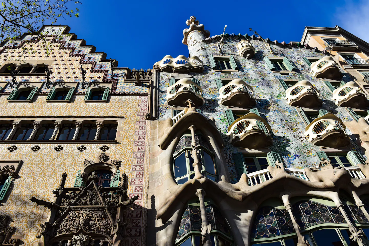 The tiled facade and mask-like balconies of Casa Batllo beside Casa Amatller on Passeig de Gracia