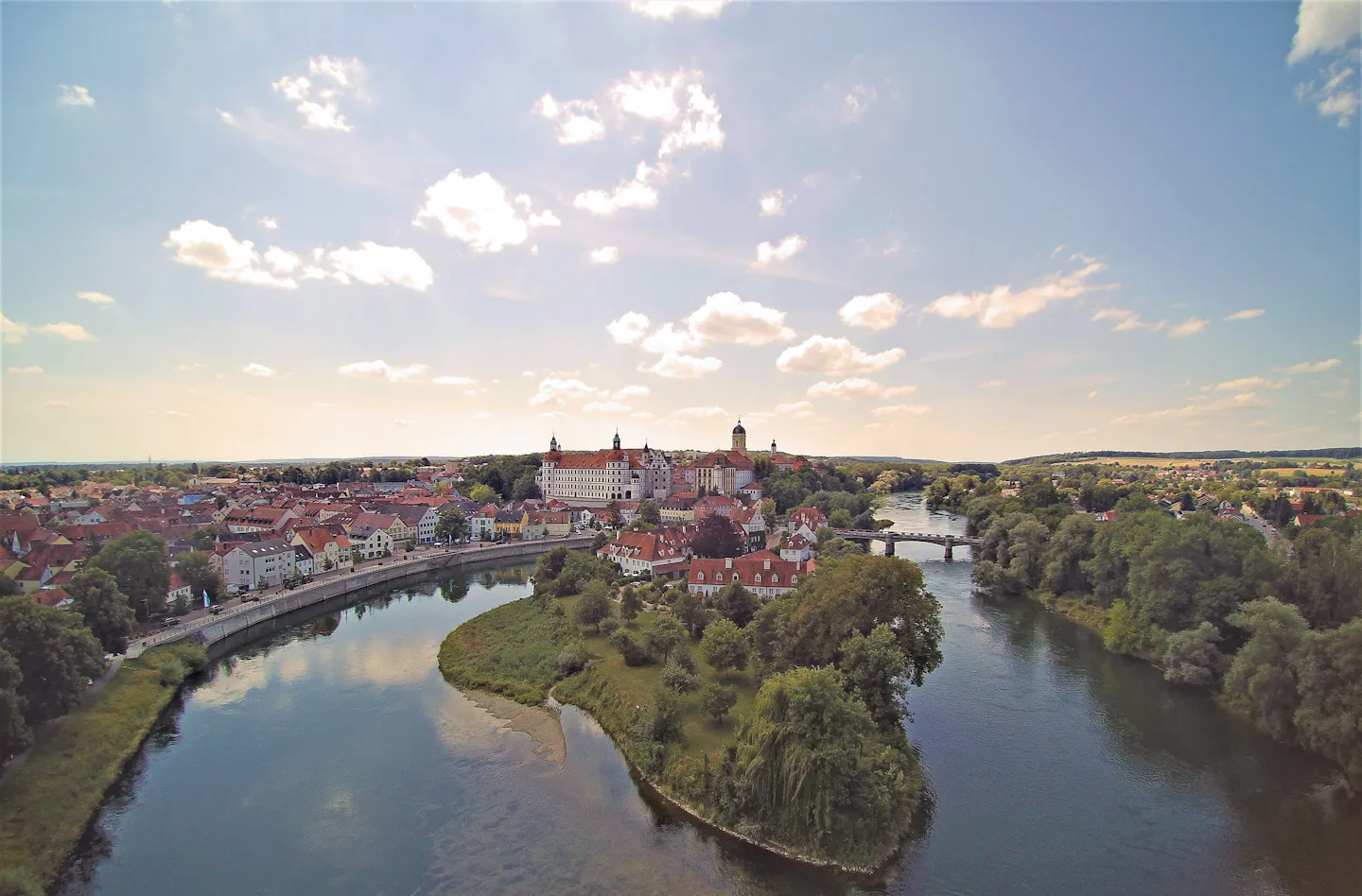 Aerial view of a historic riverside town with a large castle, clustered old buildings, bridges and surrounding countryside