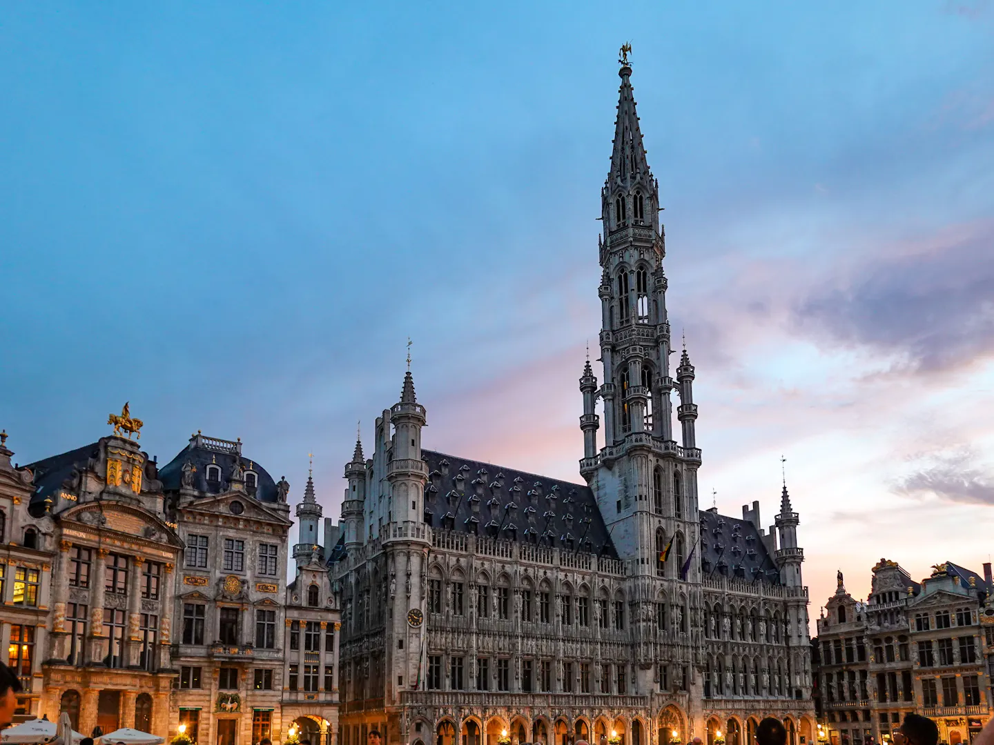 The Gothic spire of Brussels Town Hall above the lit guild houses of the Grand-Place at dusk