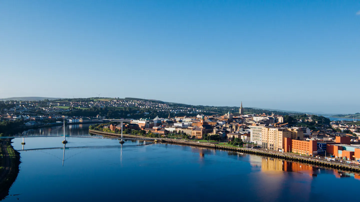Derry’s city centre and church spires above the River Foyle, with the Peace Bridge crossing the water in early morning light